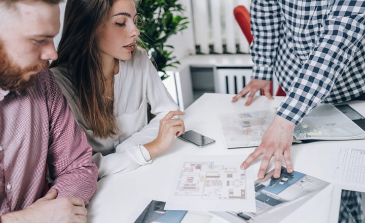 un asesor inmobiliario realizando la presentación de unos planos a una pareja